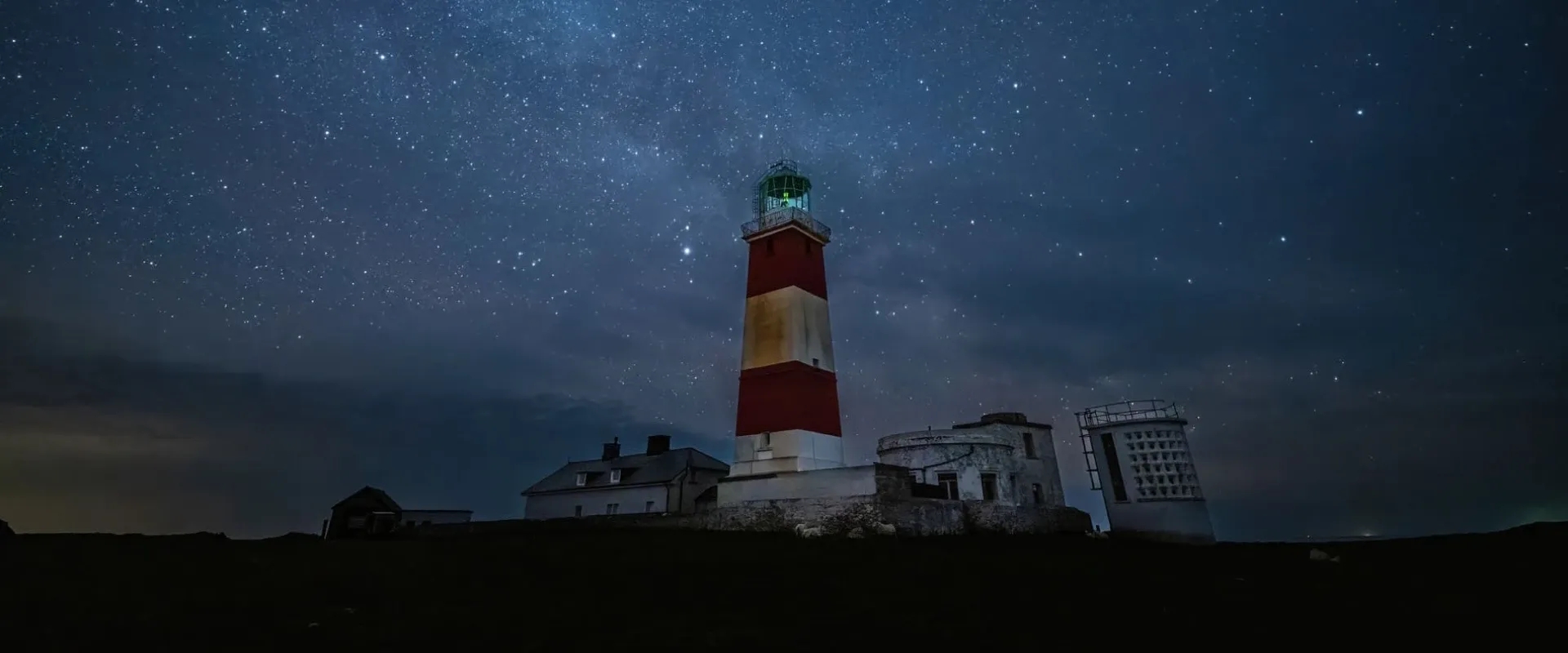 A lighthouse stands under the starry sky on Ynys Enlli in Wales